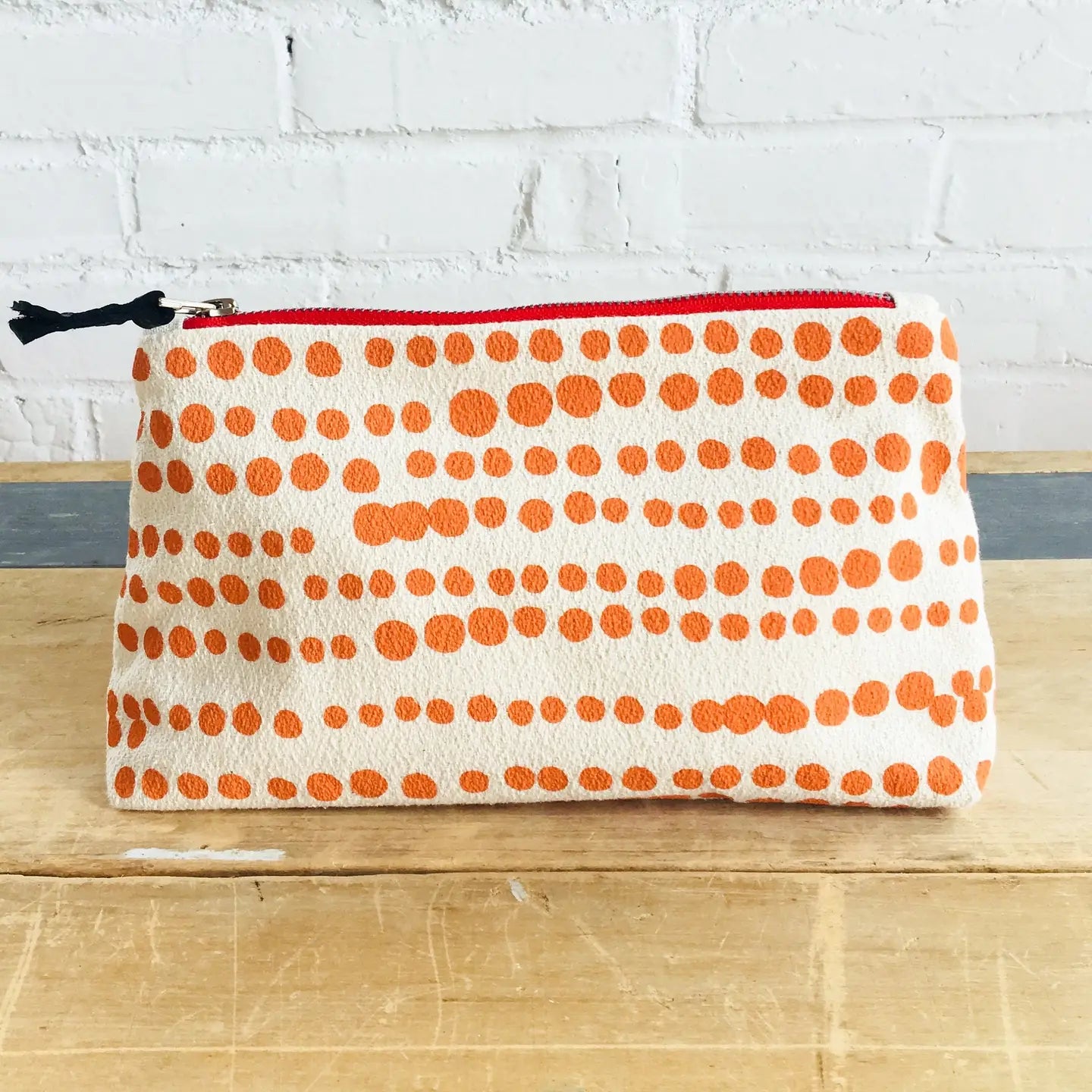 Pouch with orange polka dot pattern on a wooden surface and white brick wall background