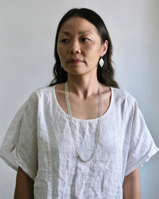 Cropped image of woman with long dark hair wearing a white round neck shirt and, silver earrings and a long silver necklace