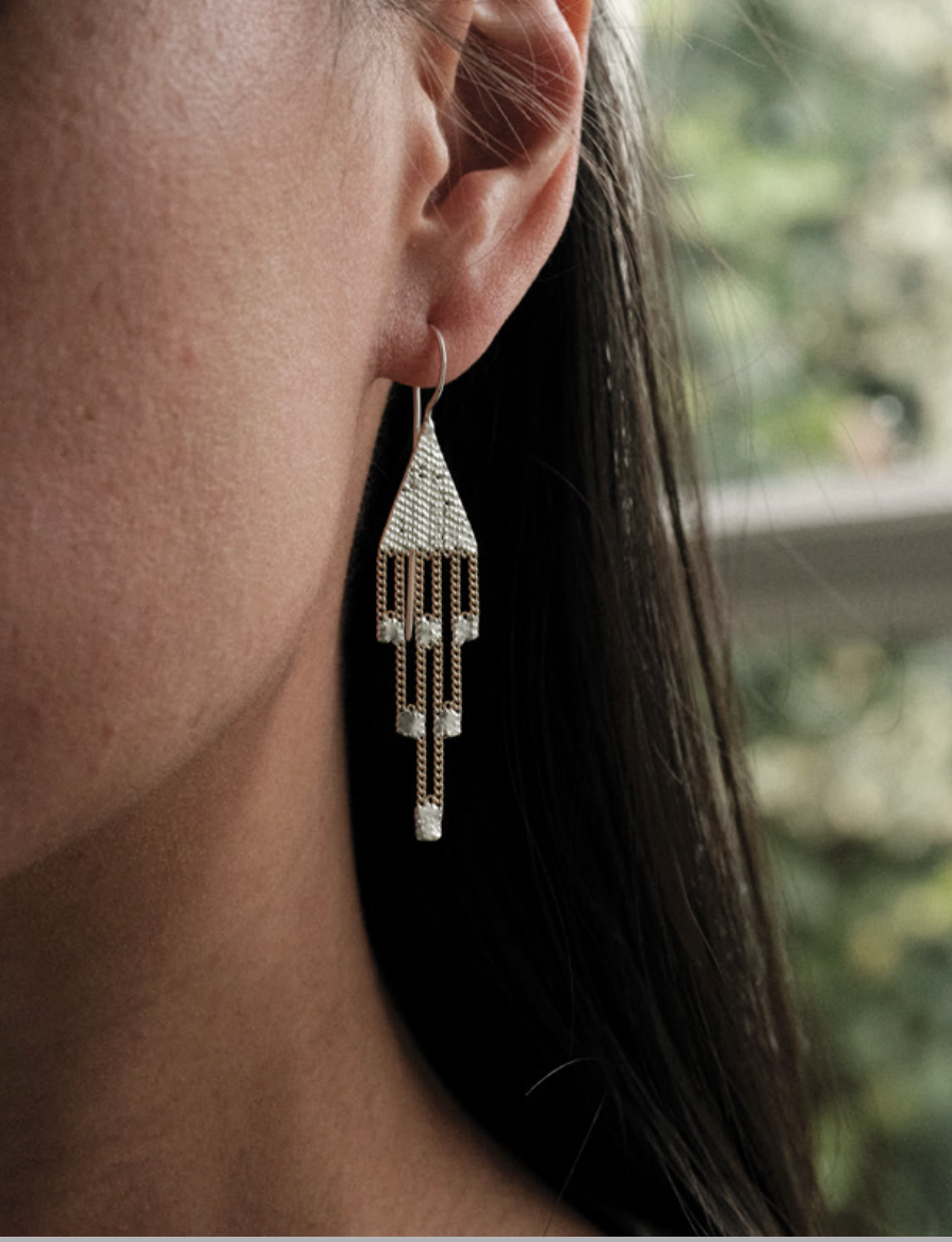 Cropped side headshot of woman with long dark hair waering a sterling silver and brass chain earring.