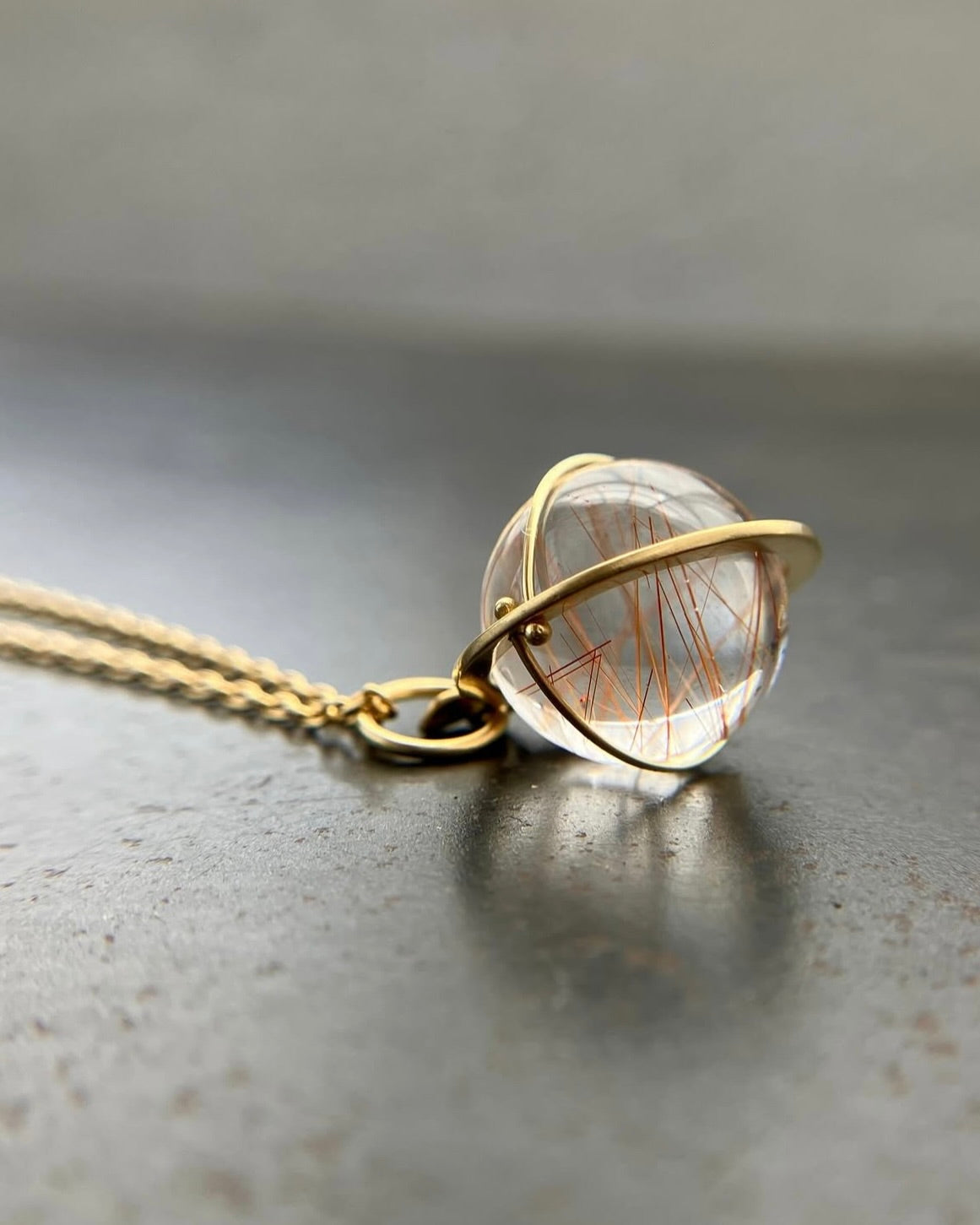 A necklace with small rutilated quartz globe set in gold on a gold chain.