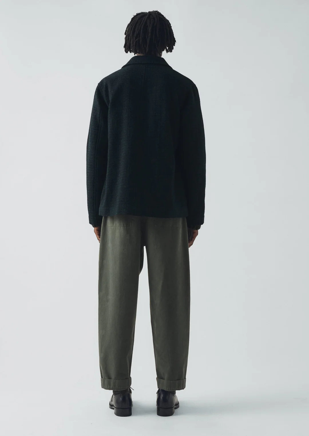 Person wearing a dark jacket and light-colored pants on a white background