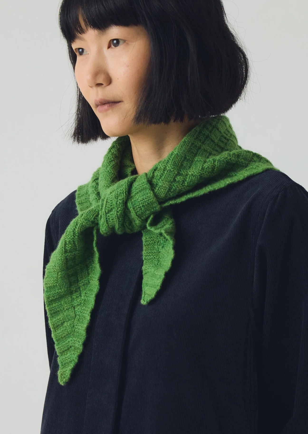 Person wearing a green knitted scarf against a plain background