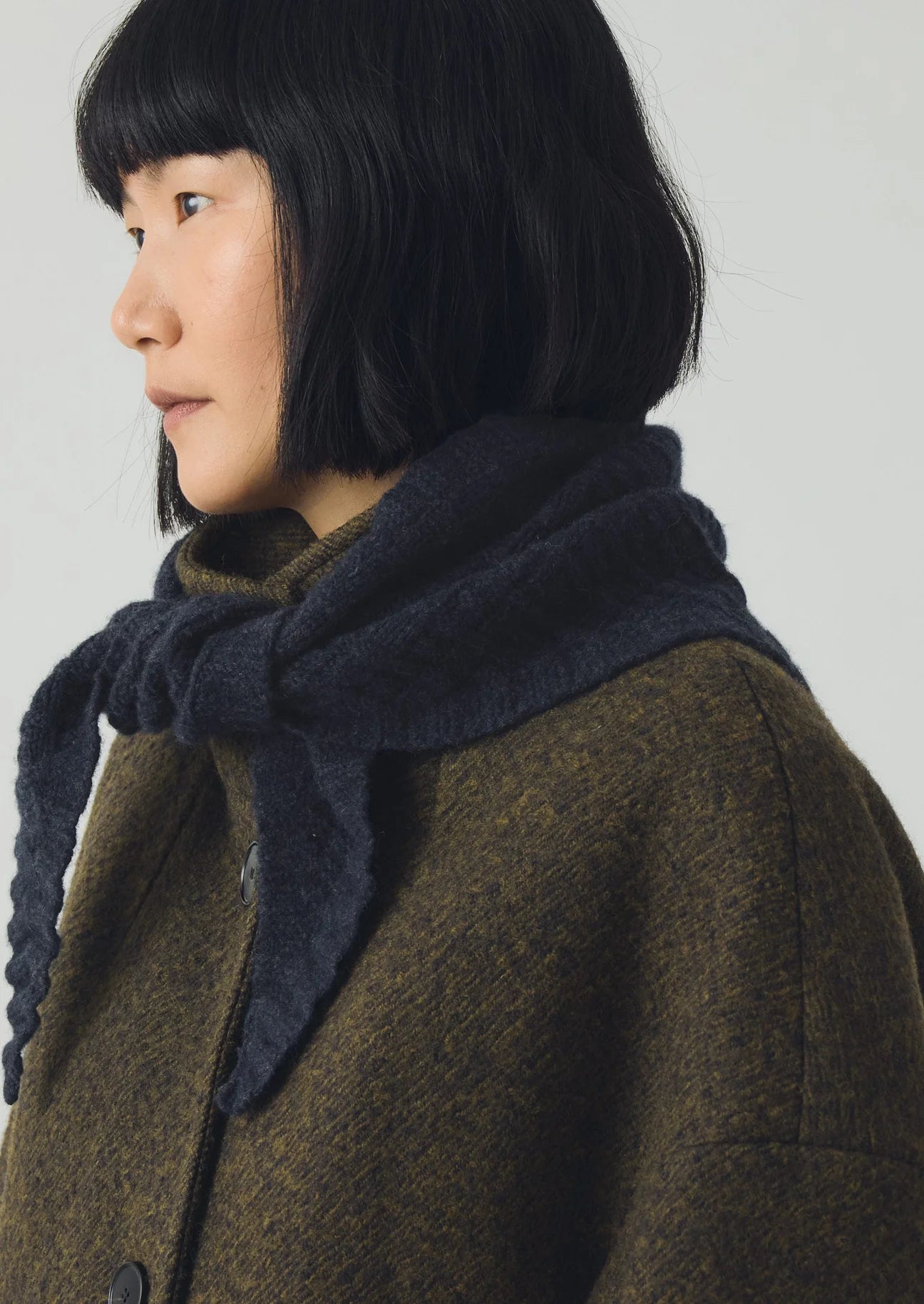 Person wearing a dark blue scarf and brown coat against a plain background