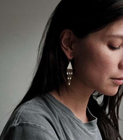 A model wearing silver and brass dangle earrings.