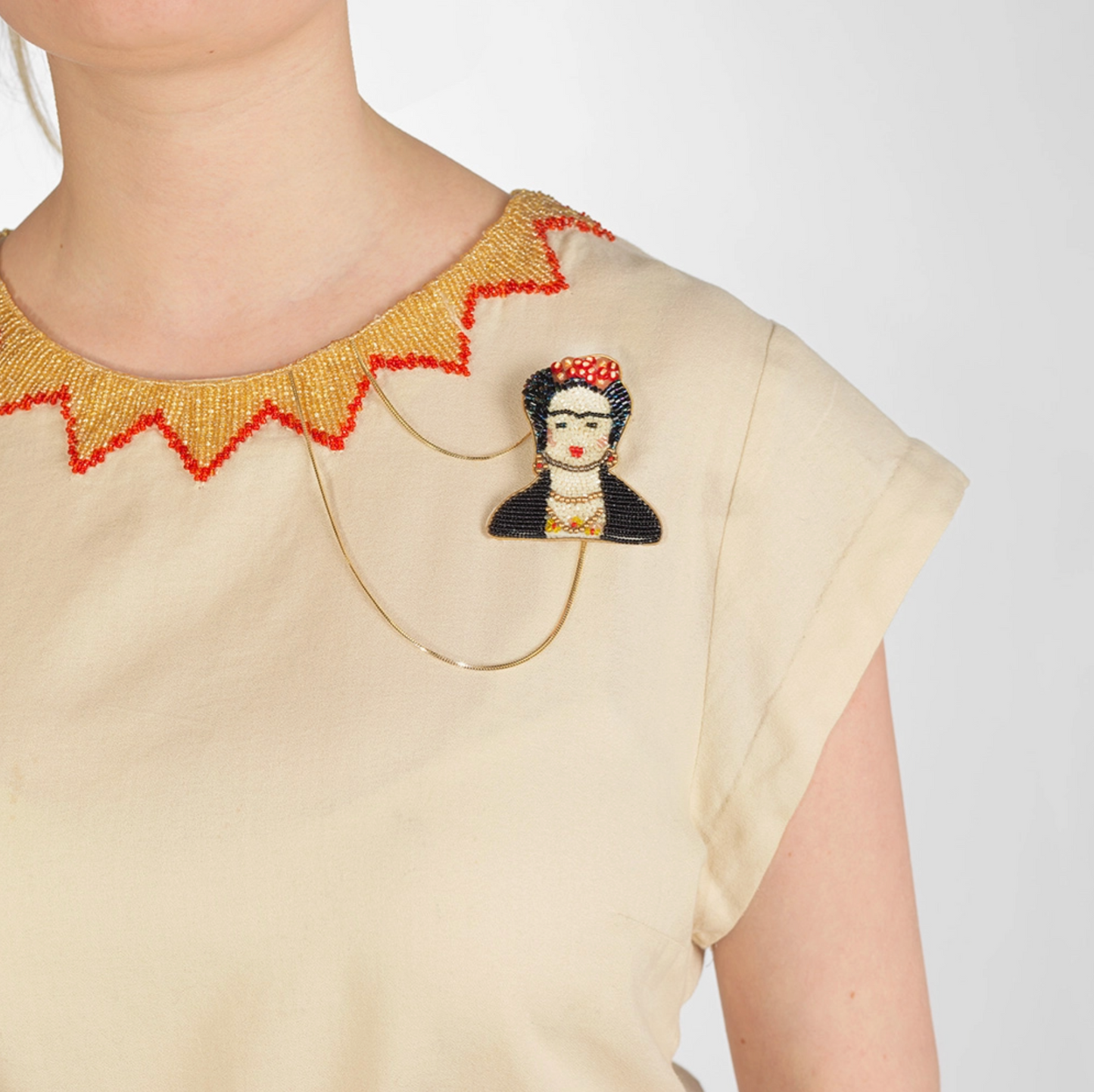 Beaded Frida Kahlo brooch pinned to cream shirt with gold beaded colar