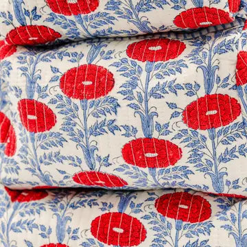 A close-up of folded quilted fabric with a repeating floral pattern in red and blue on an off-white background.