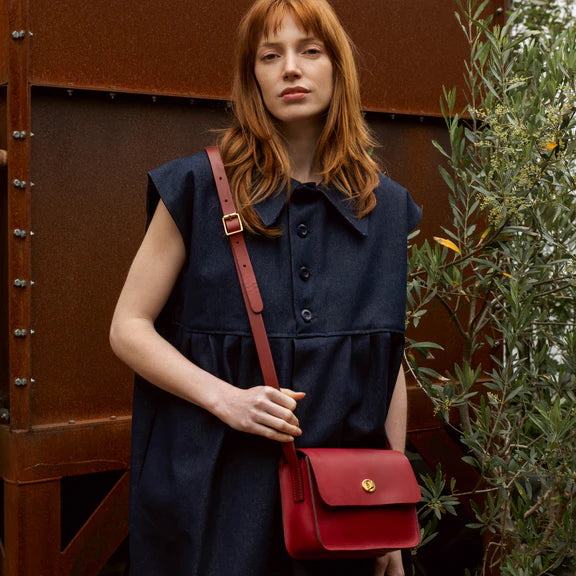 Picture of red leather handbag being worn by woman with red hair, wearing a blur dress.