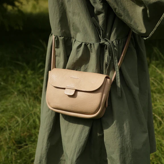 Picture, close up of person in green dress wearing a light brown handbag.