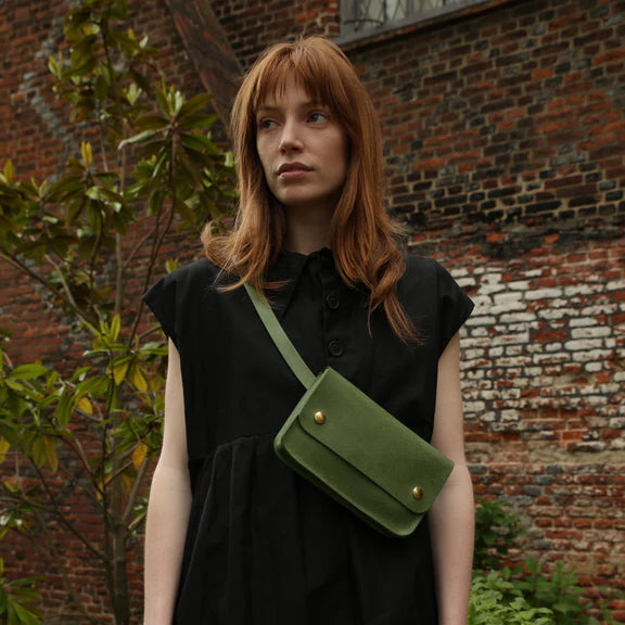 Picture of Woman with red hair and dark eyes and a black dress wearing green handbag on grey background.