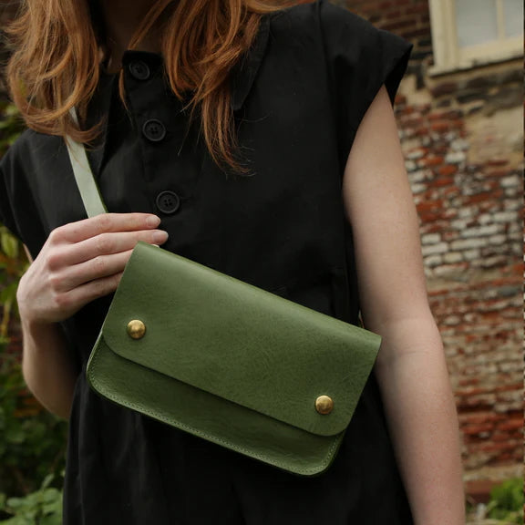 Picture, close up of Woman with red hair and dark eyes and a black dress wearing green handbag on grey background.