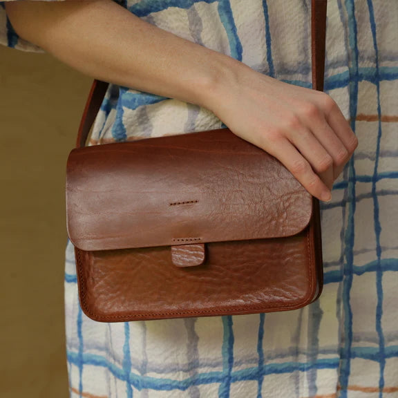 Picture, close up of the front of a brown leather handbag being worn by a person in a checked blue dress.