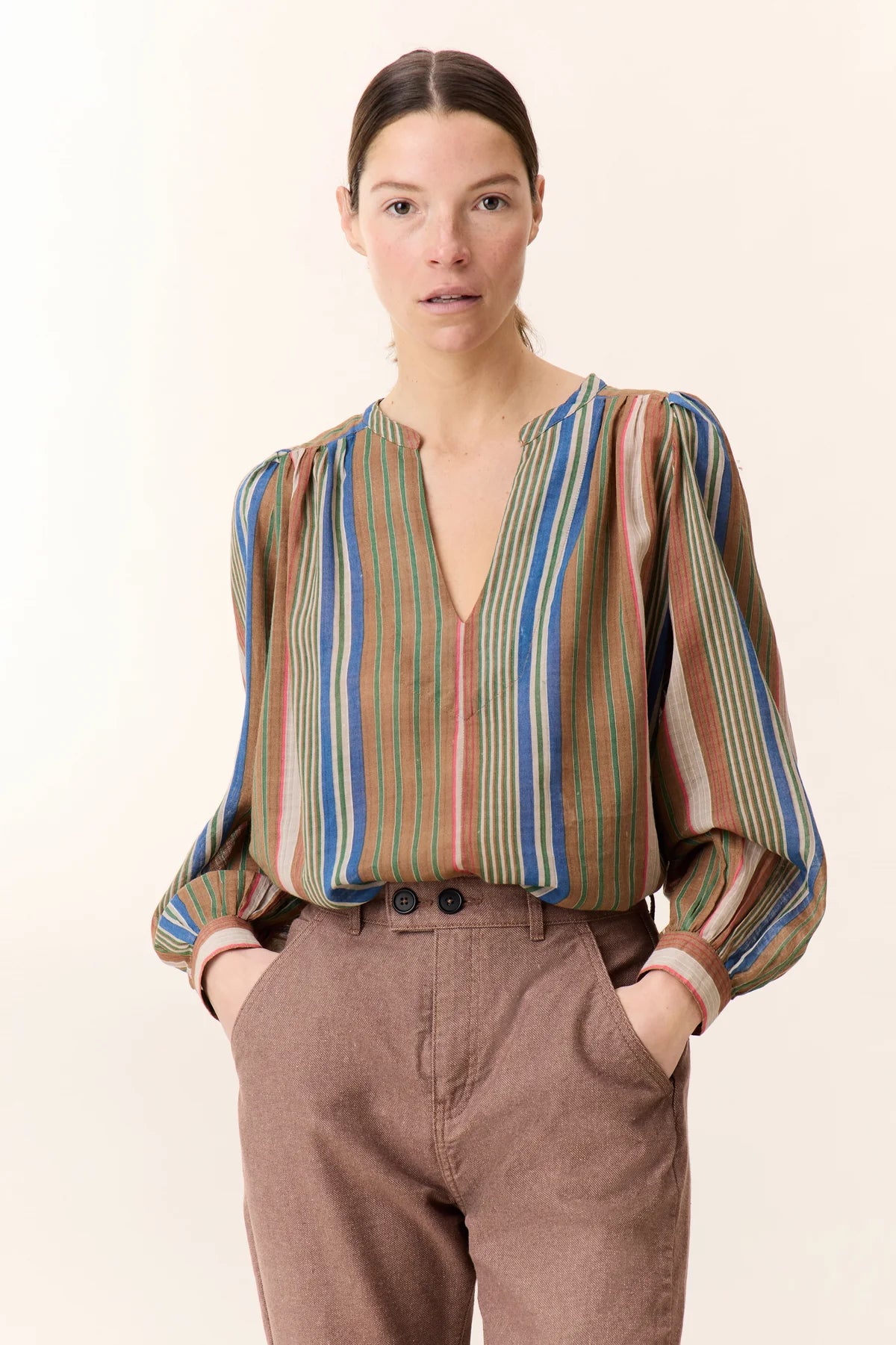 Picture 3/4 length of woman with brown hair in a pony tail and brown eyes wearing stripy top.