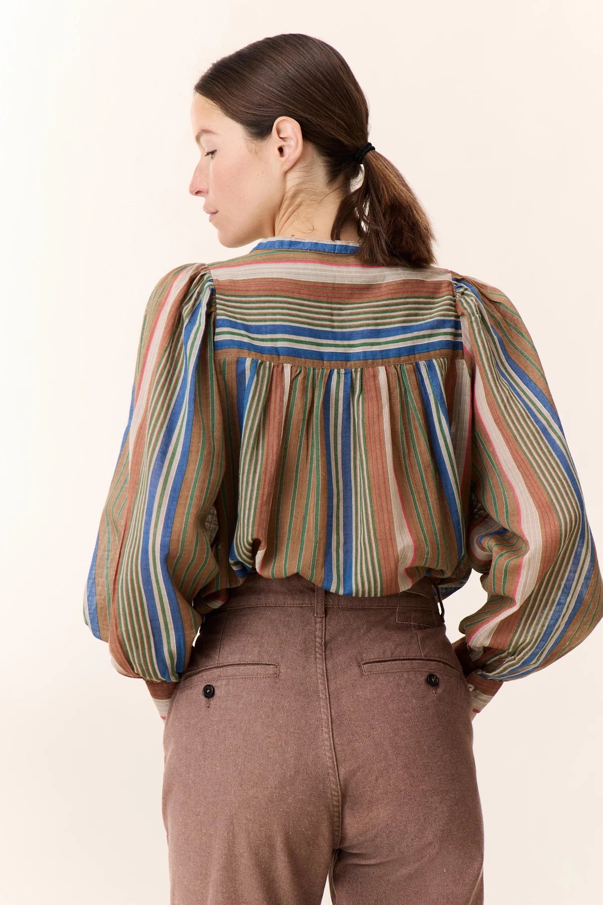 Picture of woman facing away from camera with brown hair in a pony tail and brown eyes wearing stripy top.