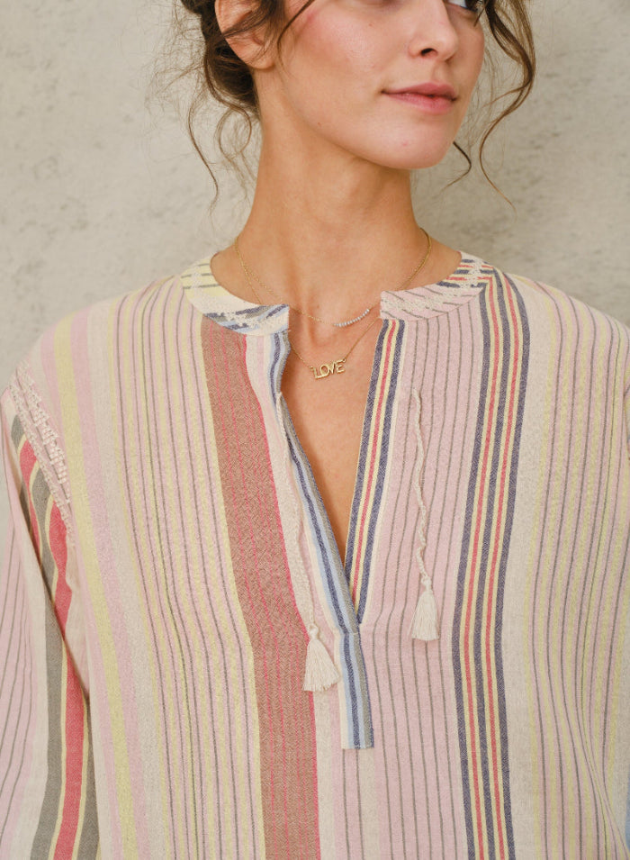 Picture of young women, close up. With curly brown hair in a bun and brown eyes. Wearing a striped dress. Against a stone-colored background.