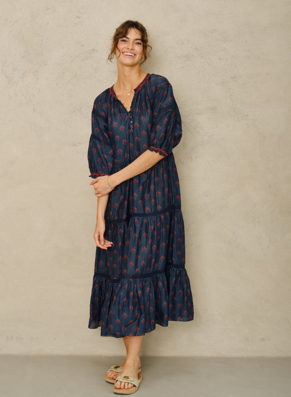 Picture, full length of woman with curly brown hair in a bun and brown eyes. Wearing a blue 3/4 length dress.