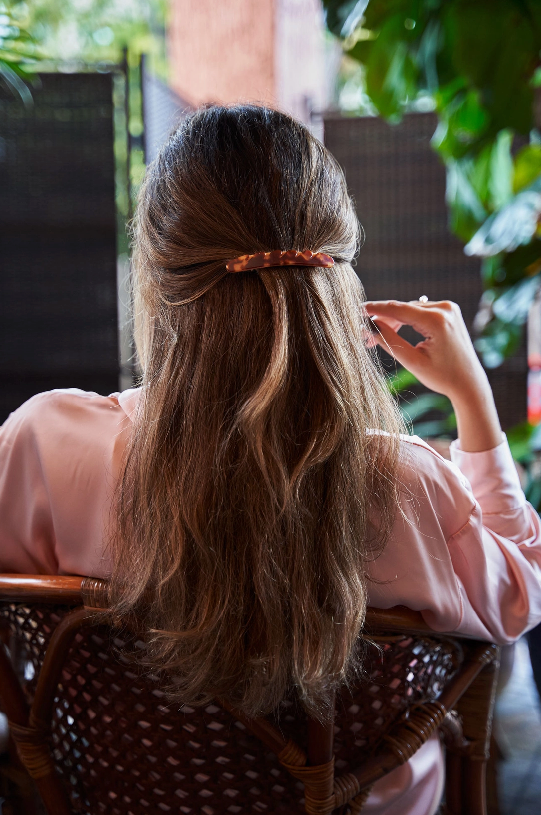 Photo of the back of a woman with long brown hair with a section of har secured with a brown baguette shaped barrette.