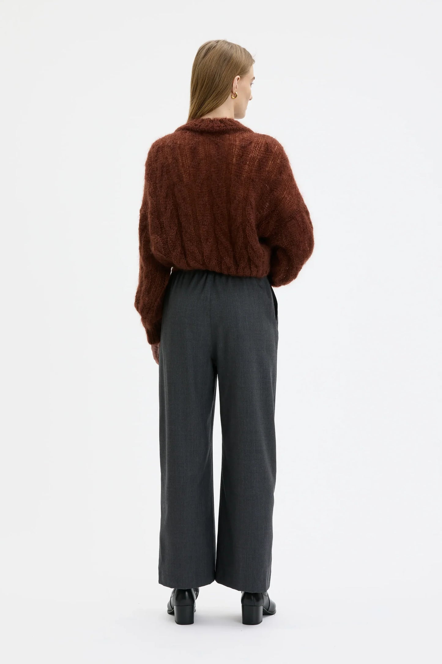 A model shown from the back wearing a brown textured cropped sweater and dark gray wide-leg trousers against a plain white studio background.