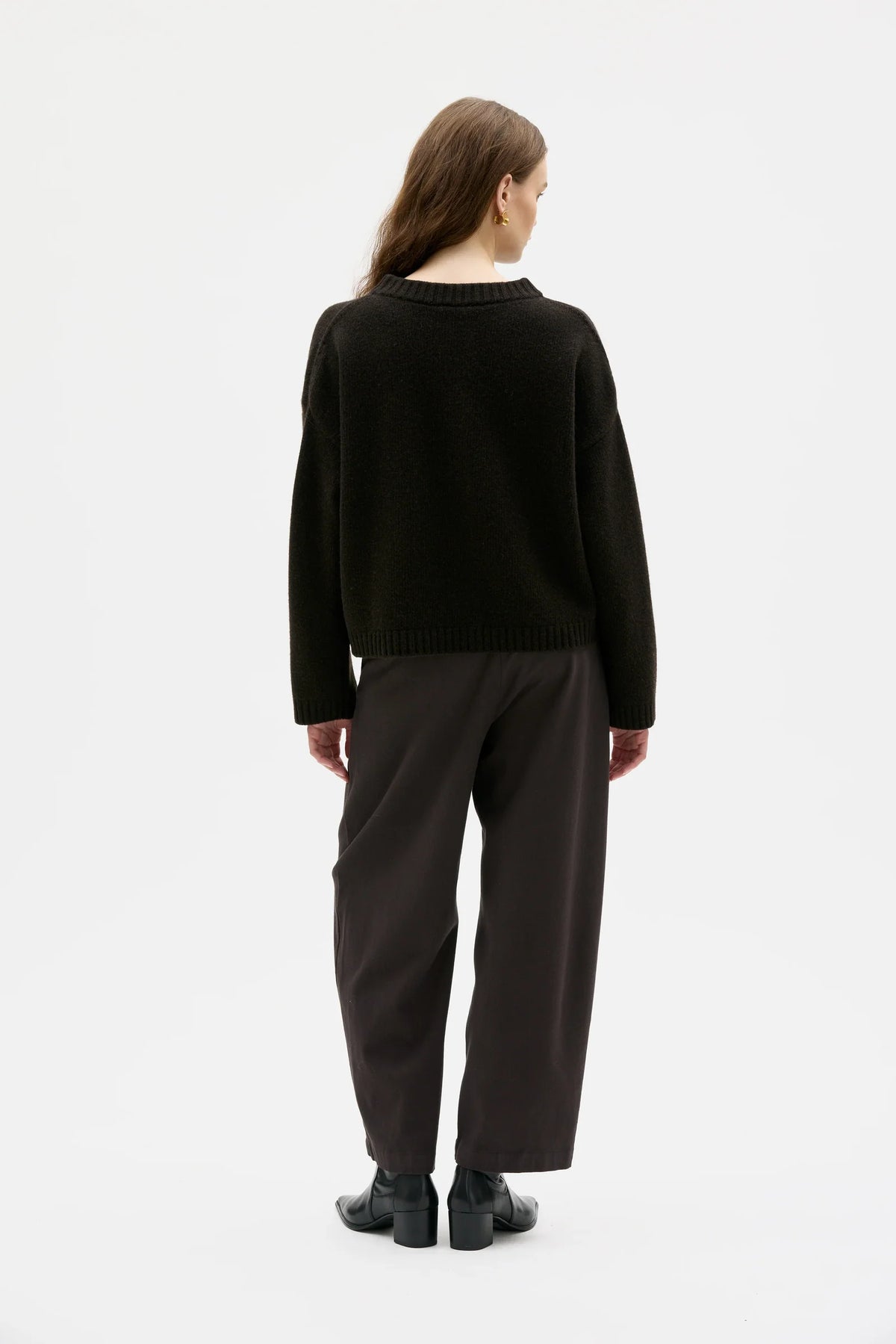 Person wearing a brown cardigan and dark pants on a white background.