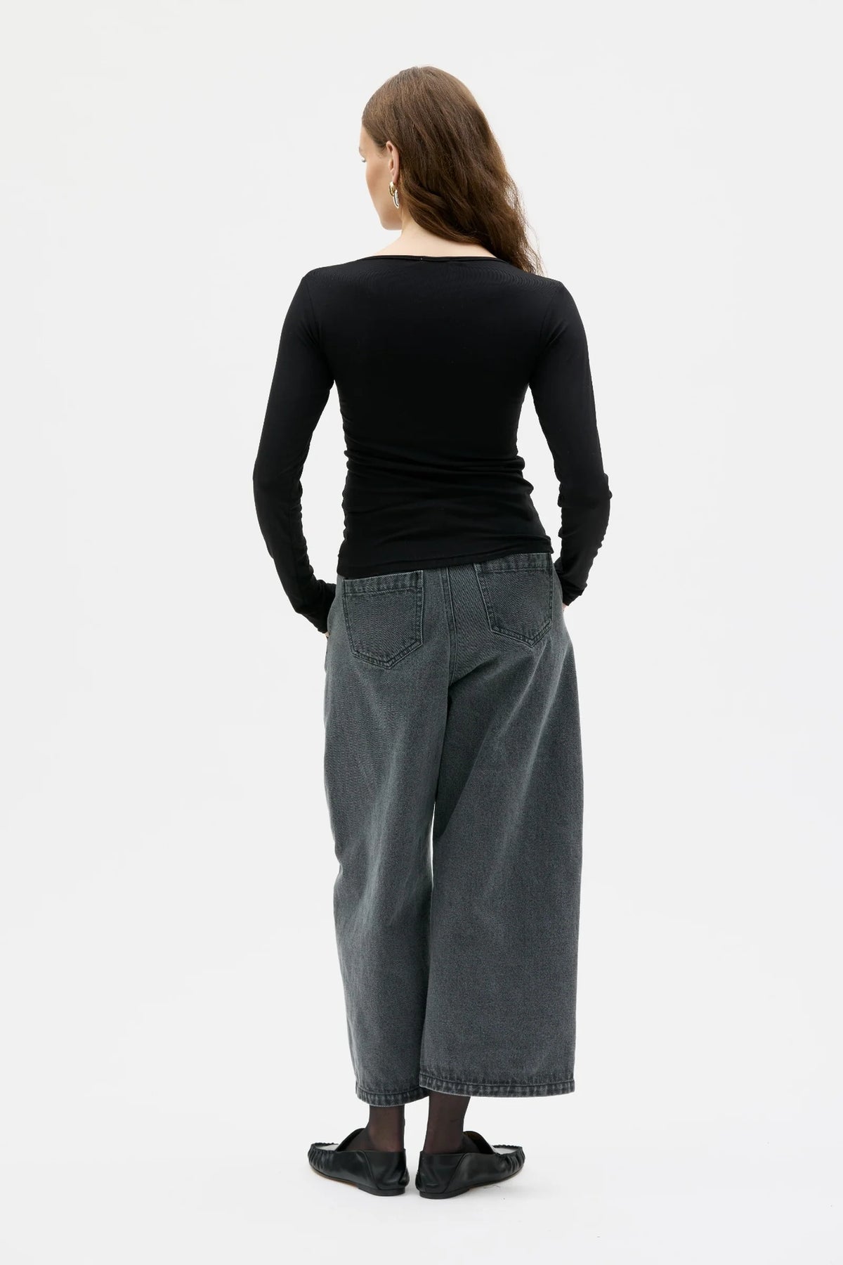 Person wearing a black long-sleeve top and gray wide-leg pants on a white background