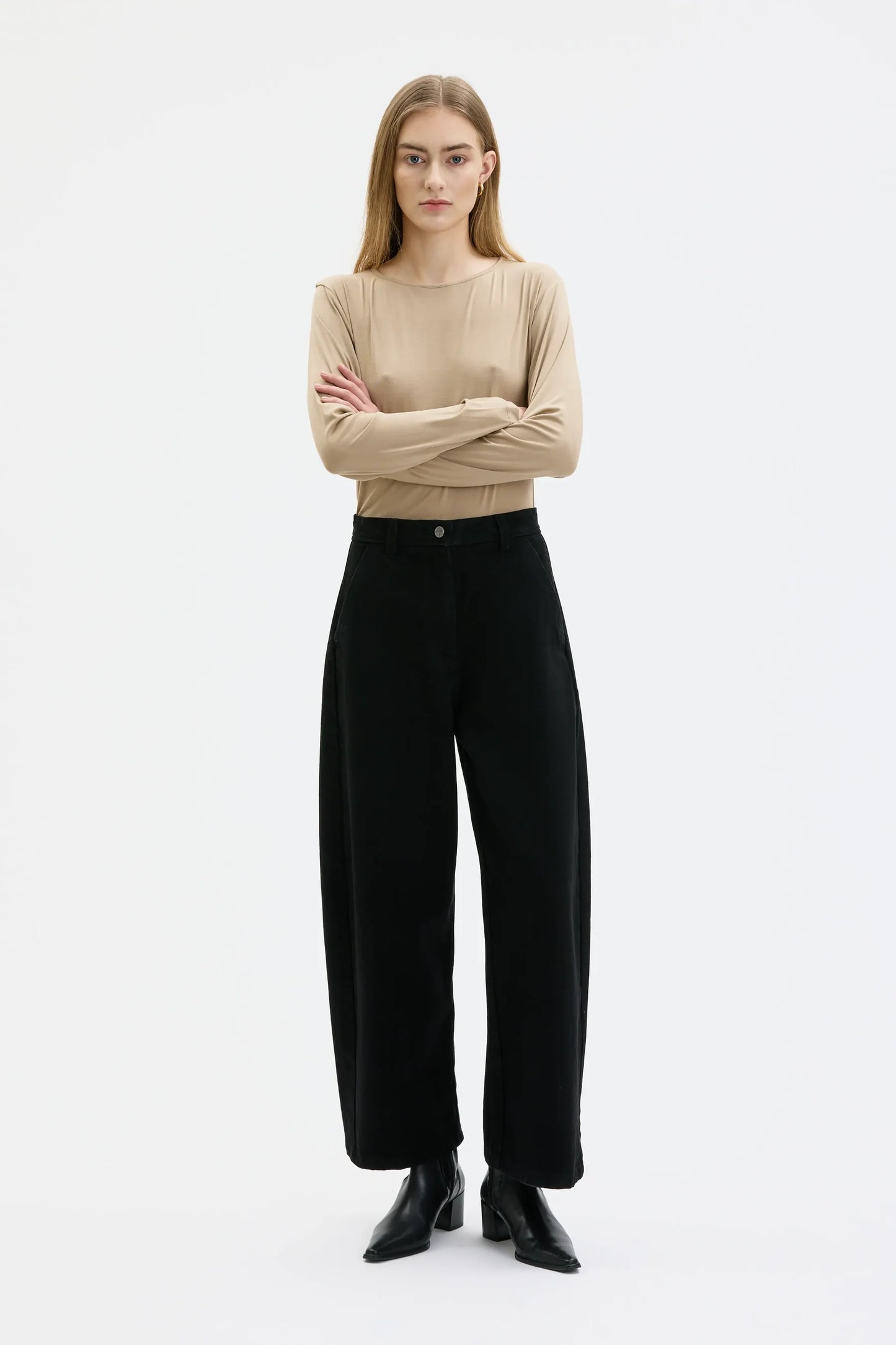 Woman wearing a beige sweater and black pants on a white background