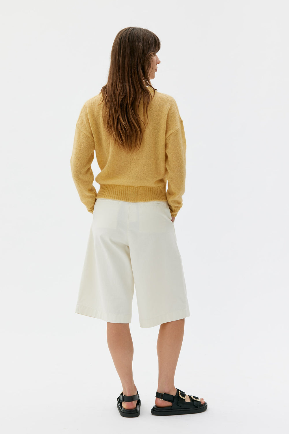 Picture, waist up of woman, facing away from camera with shoulder length brown hair and dark green eyes. wearing a yellow sweater.