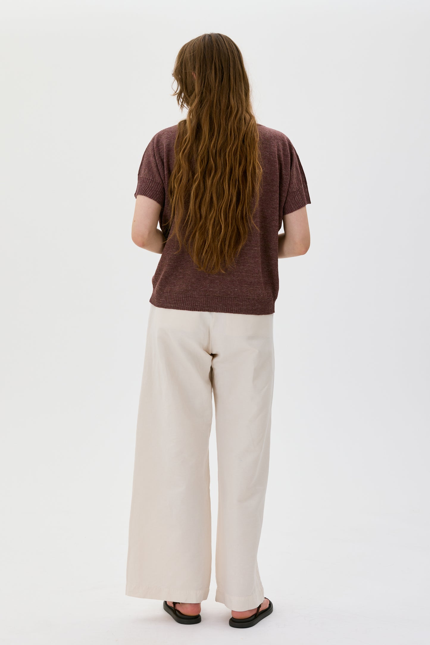 Person wearing a brown t-shirt and white pants on a white background