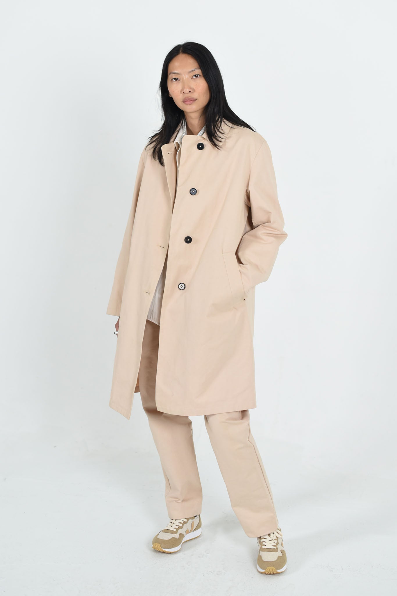 Picture of woman with Black hair and brown eyes wearing a stone clored knee length Macintosh