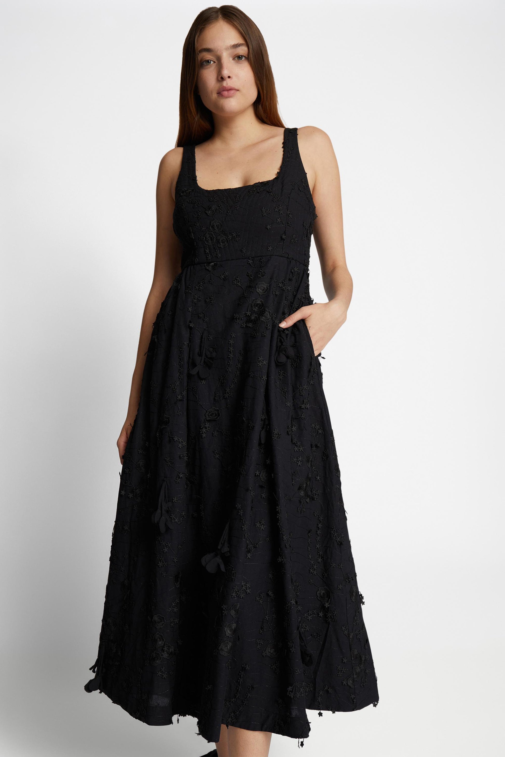 Woman wearing a black dress with narrow straps embellished with floral applique all over.