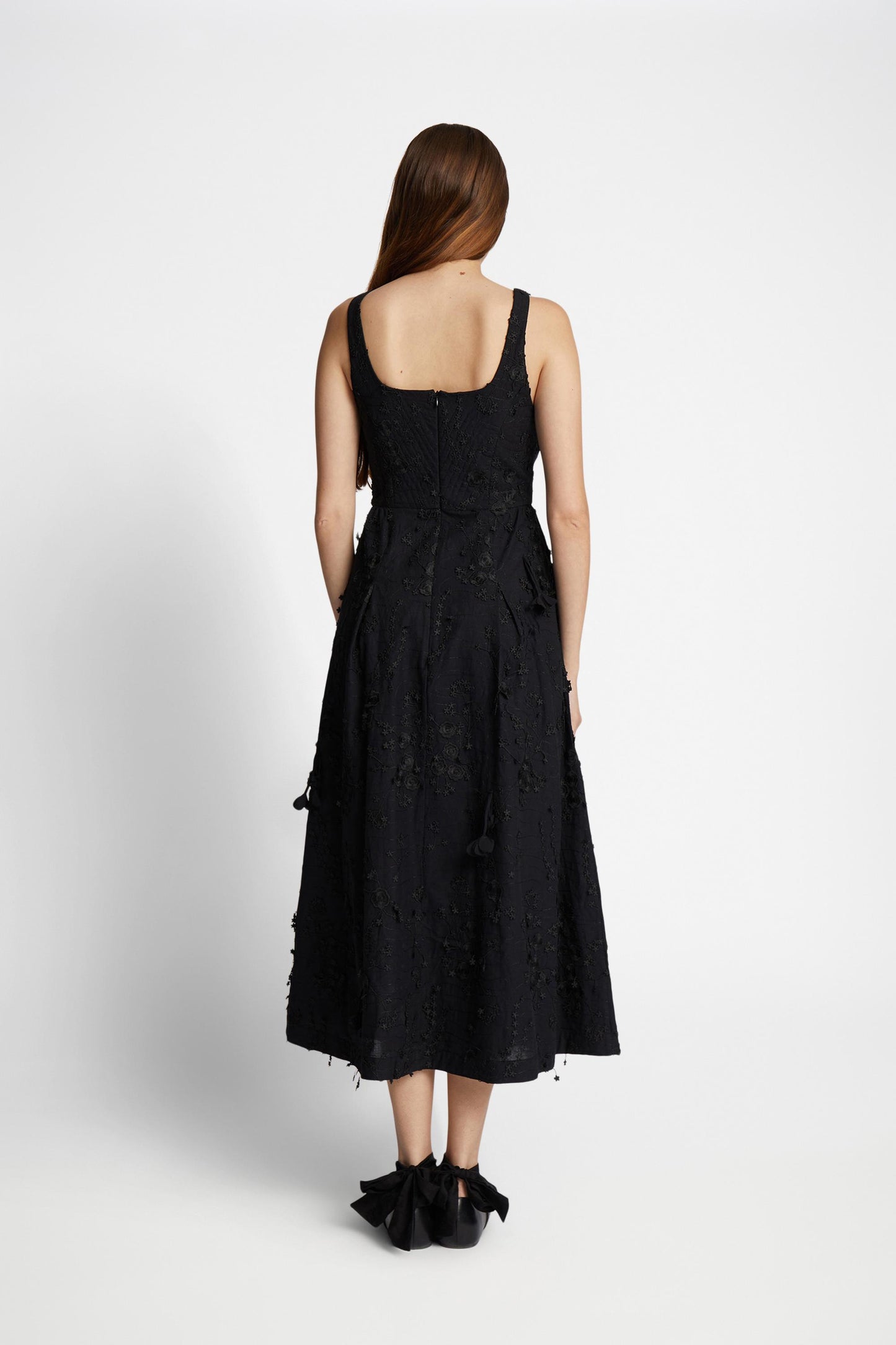 Reverse view of a woman wearing ablack dress with narrow straps embellished with floral applique all over.