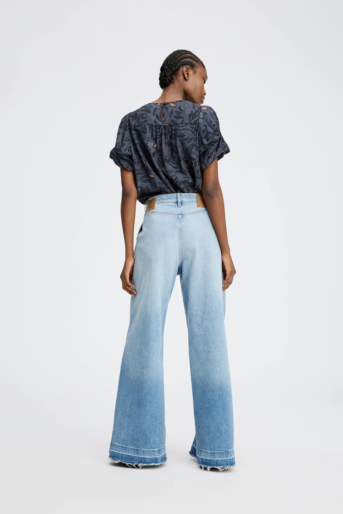 Person wearing a patterned top and light blue jeans on a white background