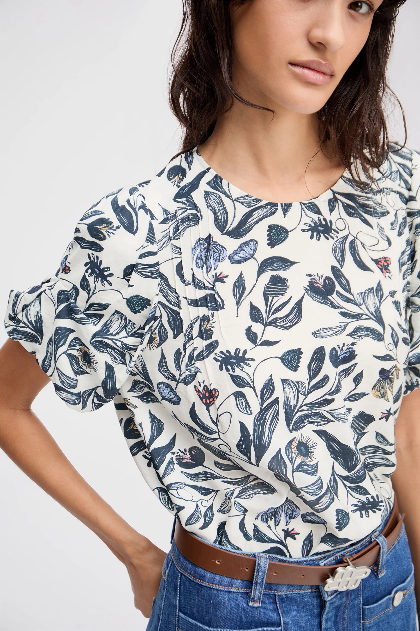 Woman wearing a white blouse with blue floral pattern and blue jeans on a plain background