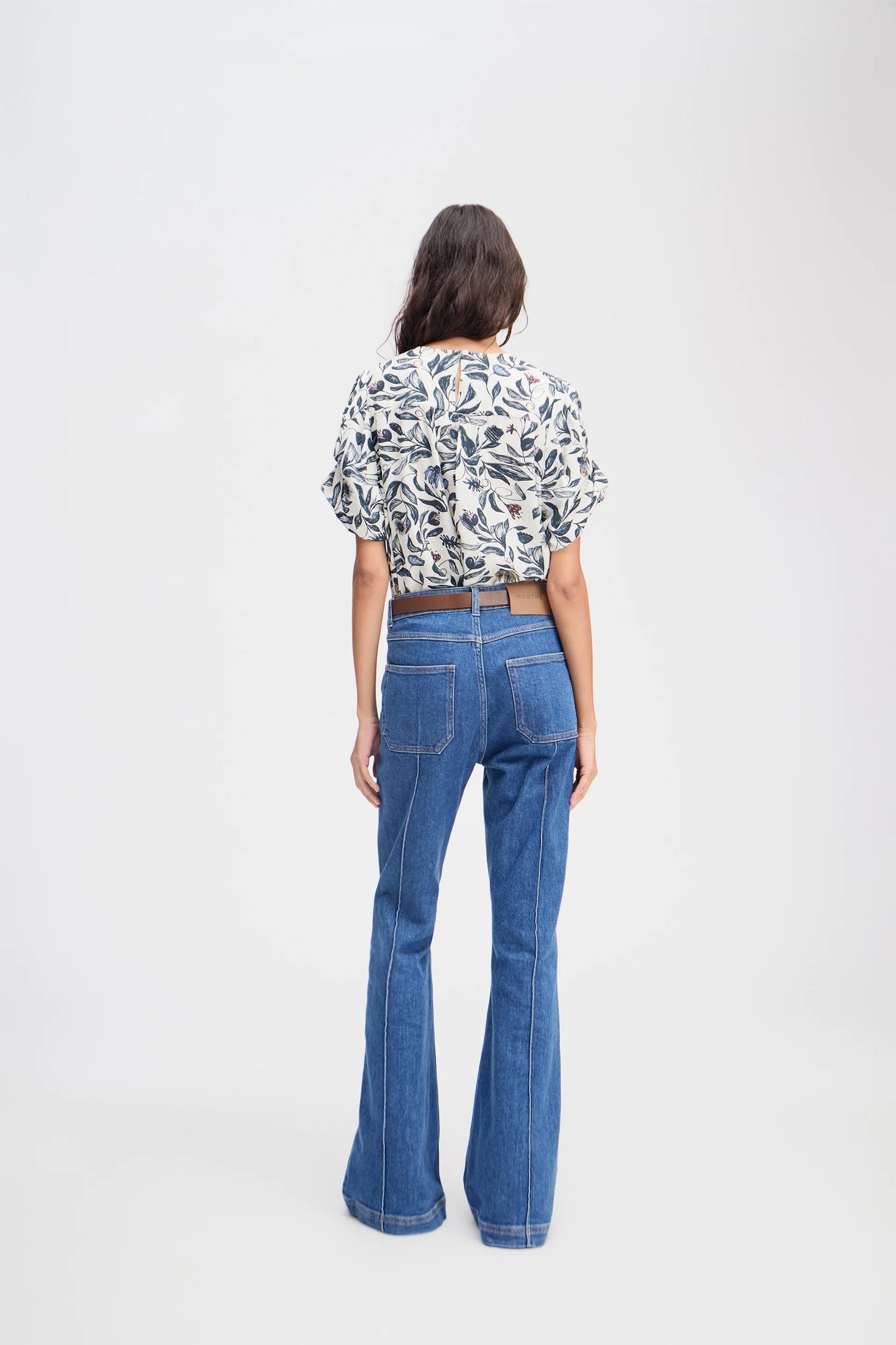Person wearing a floral blouse and blue jeans on a white background