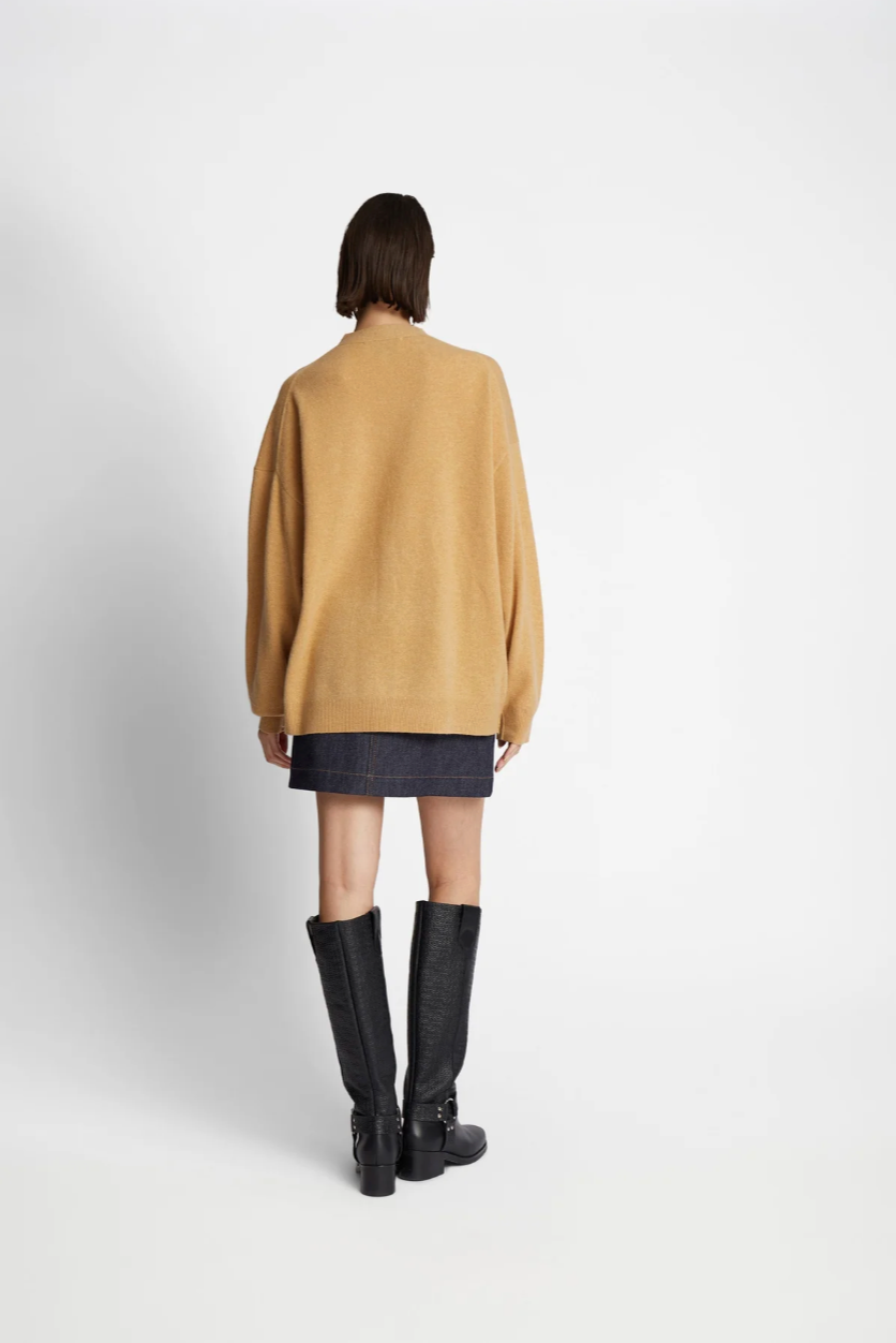 Rear view of woman modeling light camel colored cardigan with black short skirt and black knee length boots