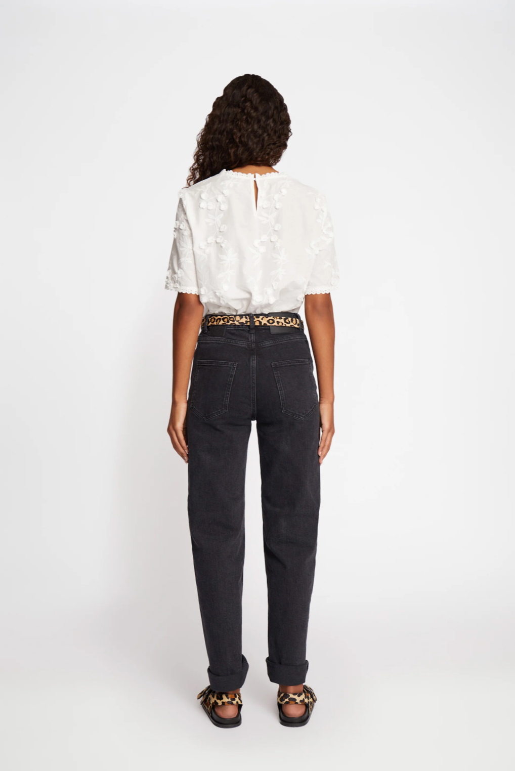 Rear view of oman with long dark wavy hair wearing white round neck blouse with floral decoration.