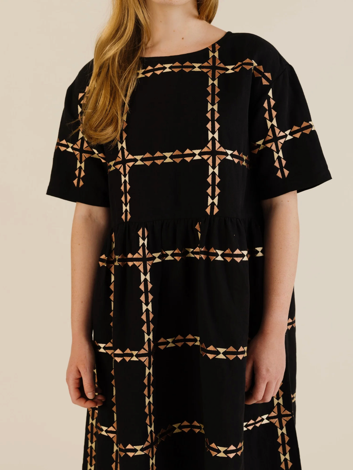 Black dress with geometric pattern worn by a person on a beige background
