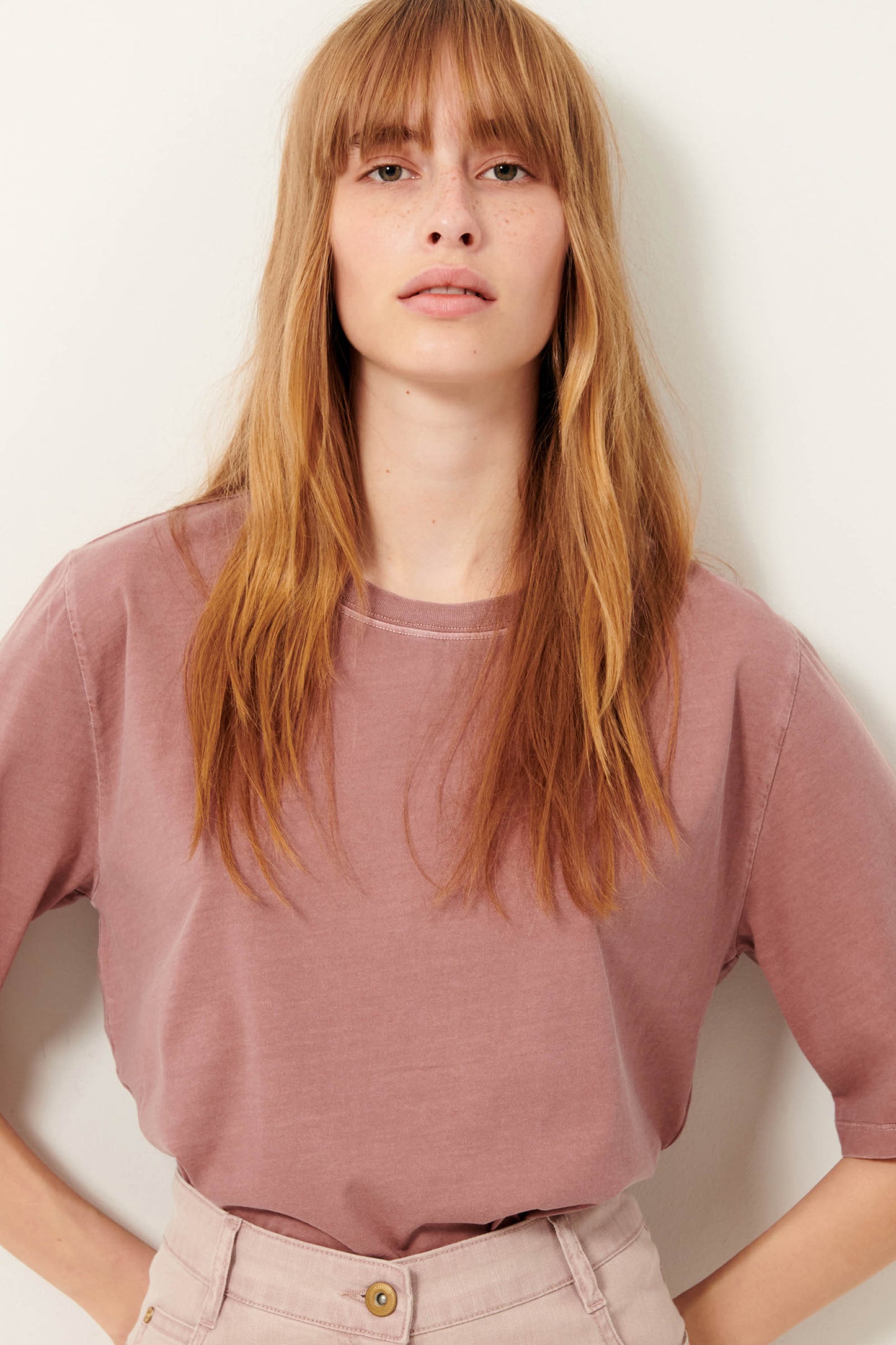 Picture of young woman from waist up. she has read hair and dark green eyes. wearing a rise colored short sleeve tee shirt.