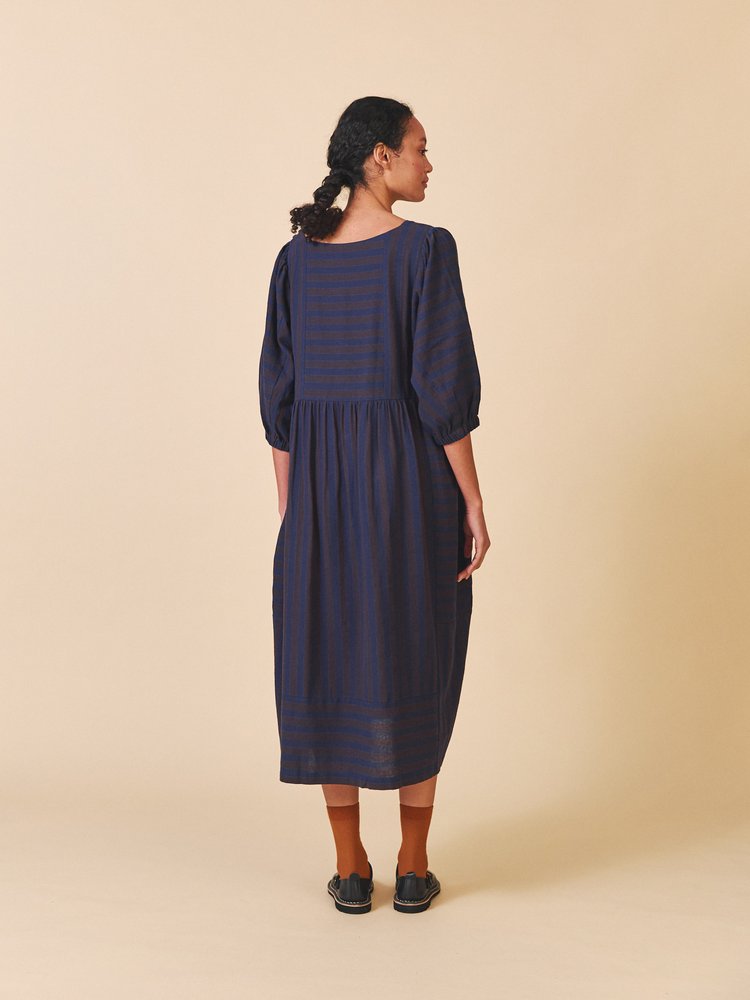 Woman wearing a dark blue dress with striped pattern on a beige background