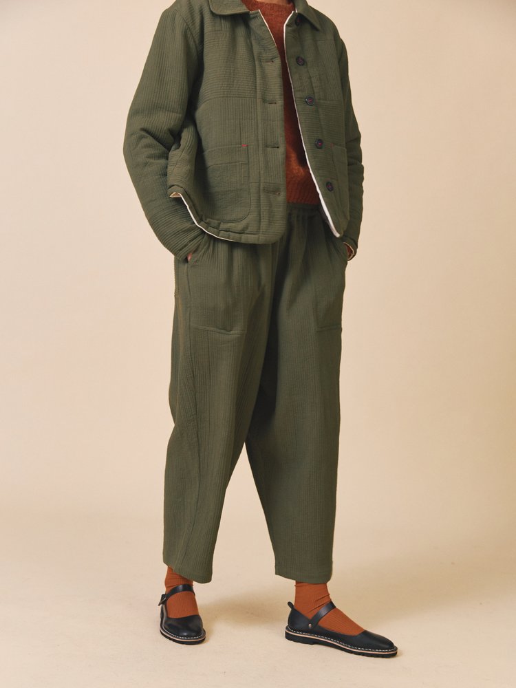 Person wearing a green outfit with a jacket and pants on a beige background
