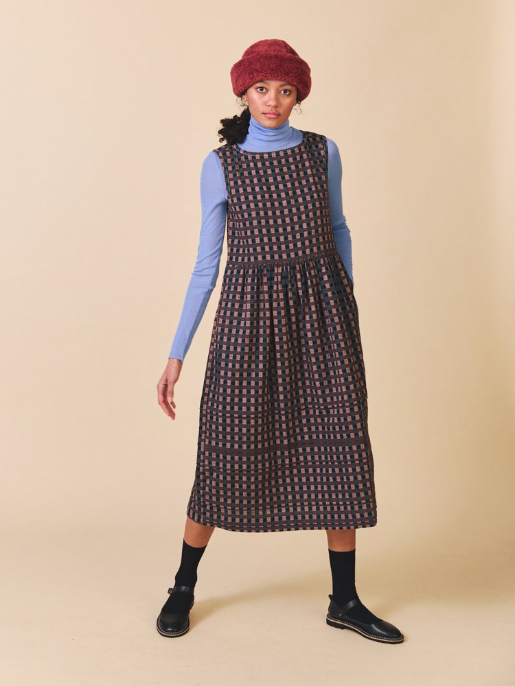 Woman wearing a patterned dress with a blue sweater and red beret on a beige background
