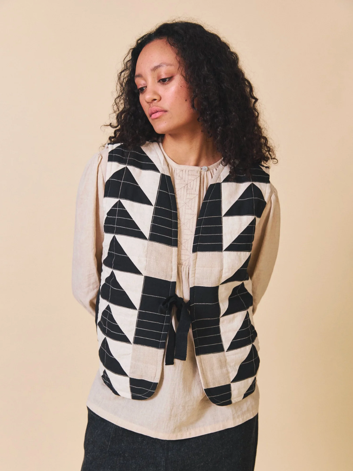 Woman wearing a geometric patterned vest over a plain shirt against a beige background