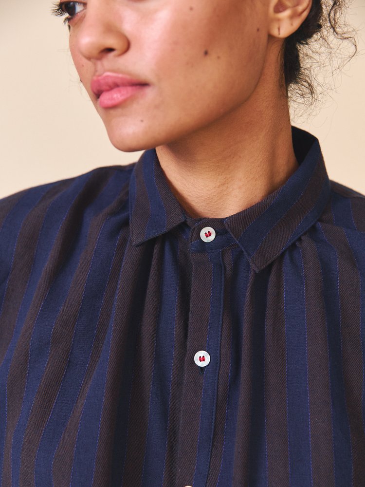 Close-up of a person wearing a navy blue striped shirt with a beige background