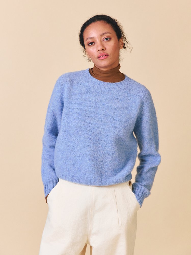 Woman wearing a blue sweater and white pants against a beige background