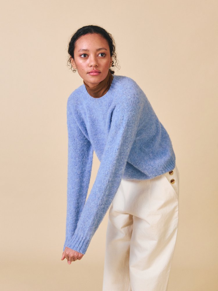 Woman wearing a light blue sweater and beige pants against a beige background
