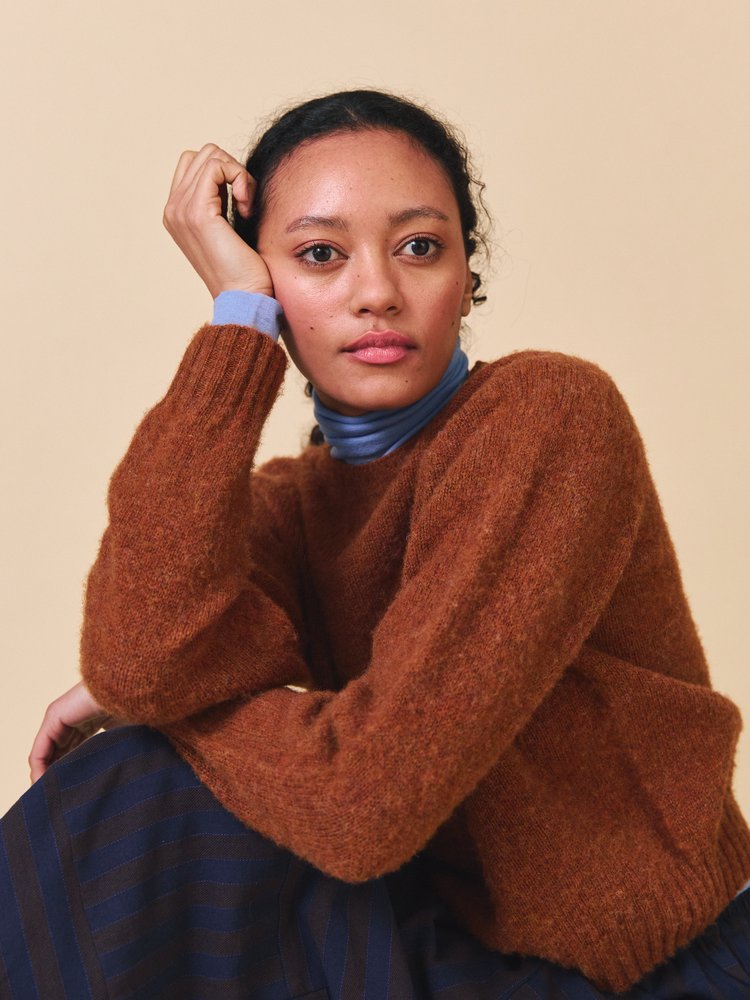 Woman wearing a brown sweater over a blue turtleneck against a beige background