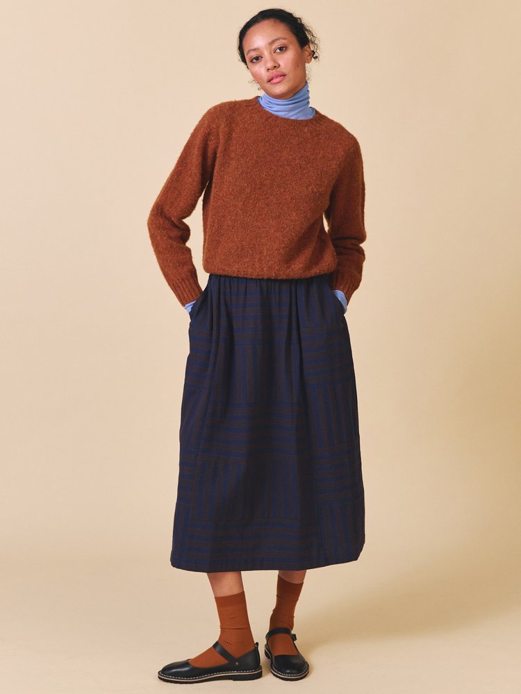 Woman wearing a brown sweater and navy skirt against a beige background