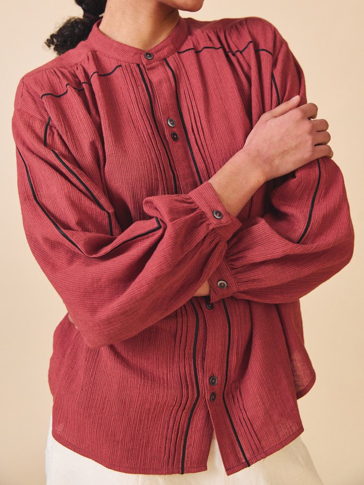 Red blouse with black trim worn by a person on a beige background