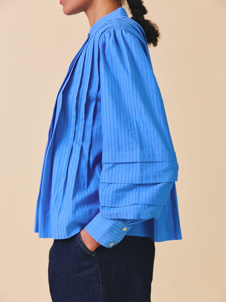 Person wearing a blue layered blouse against a beige background