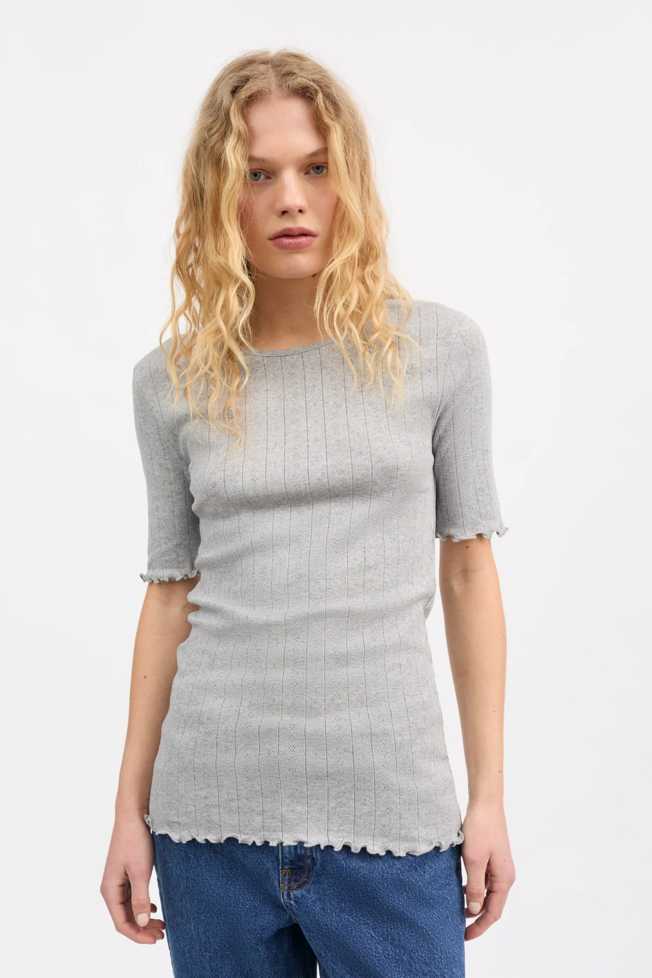 Woman wearing a gray ribbed sweater and blue jeans on a white background
