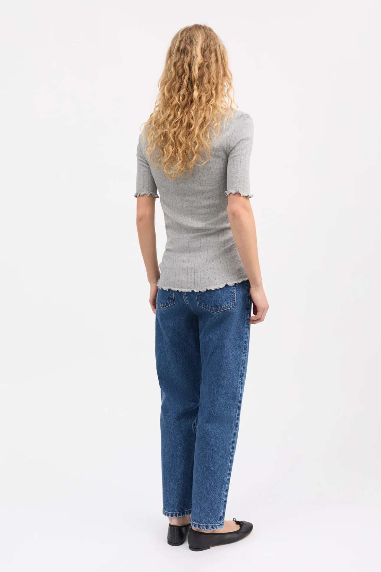 Person wearing a gray striped shirt and blue jeans on a white background