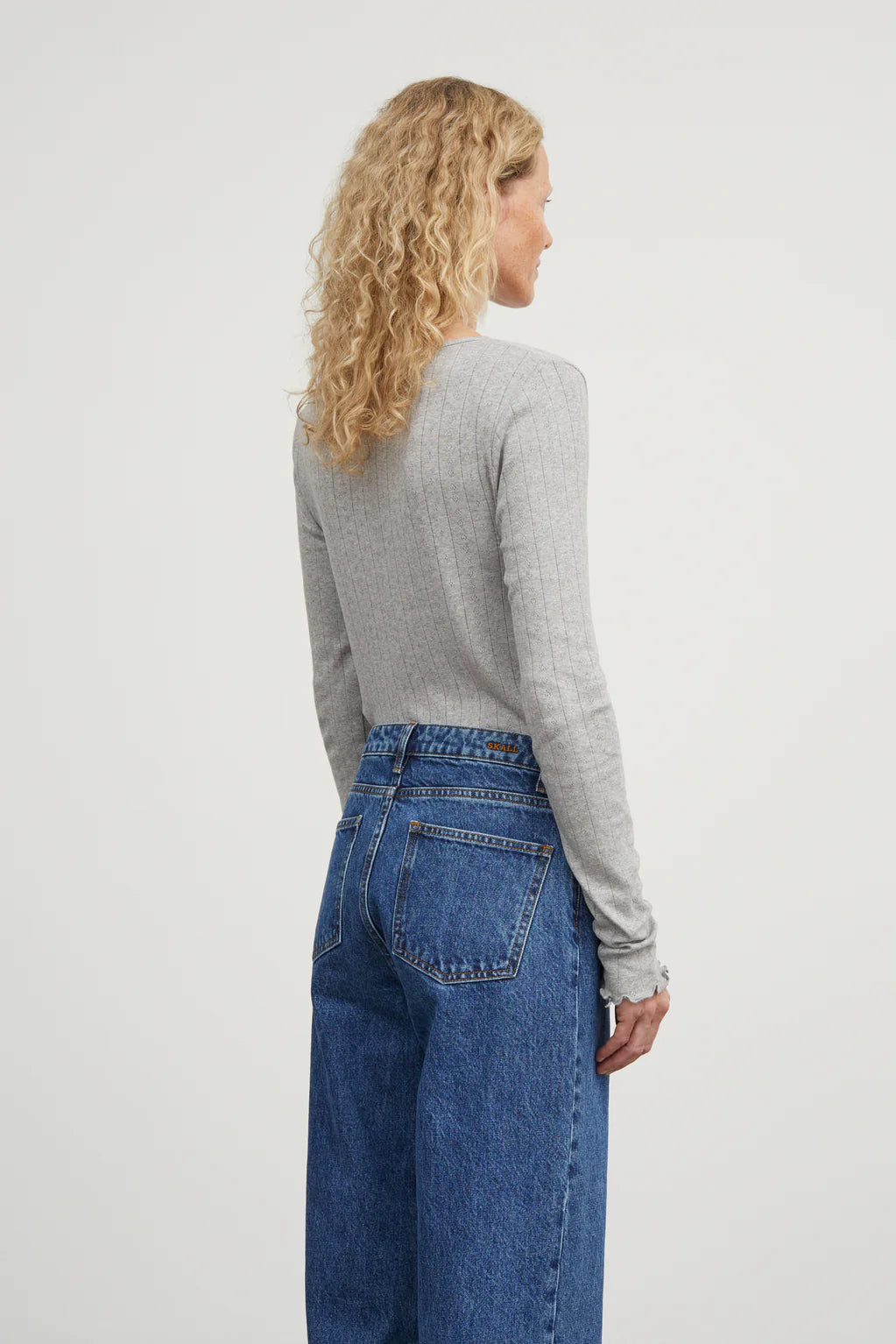 Person wearing a gray sweater and blue jeans on a white background
